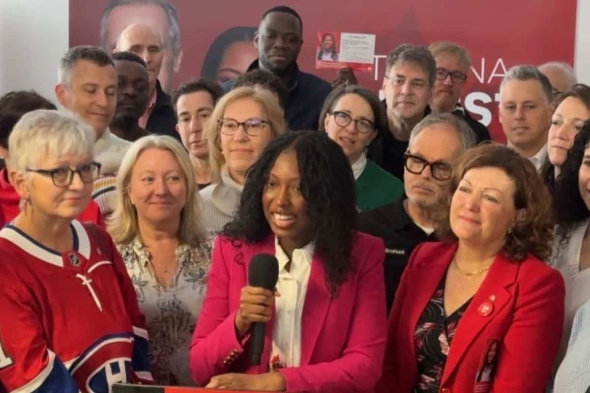 Groupe rassemblé devant un fond rouge; une personne parle au micro lors d’un événement ou point de presse intérieur.