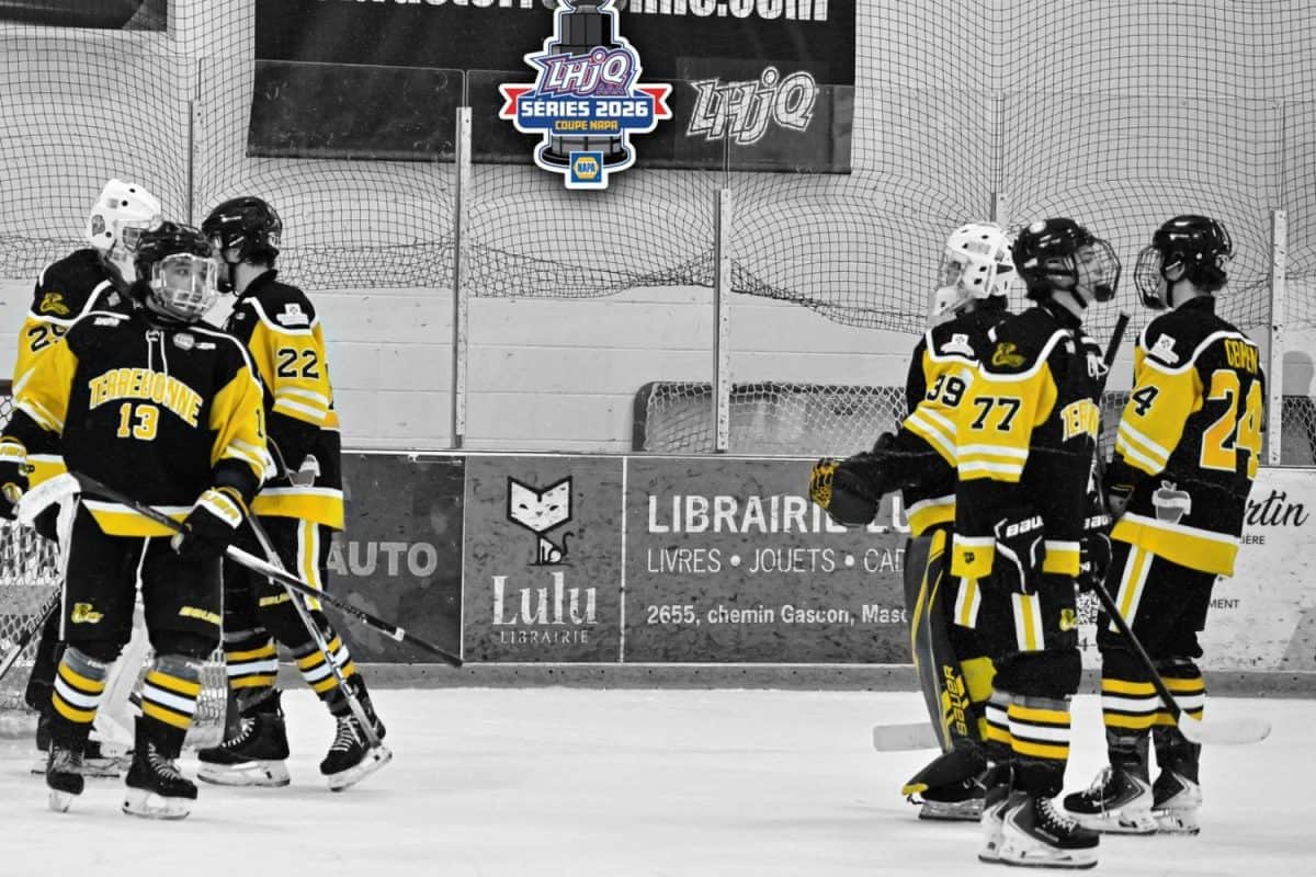 Patinoire intérieure avec bandes, filet de protection et affiches. Des joueurs en tenue de hockey se regroupent sur la glace après une séquence de jeu.