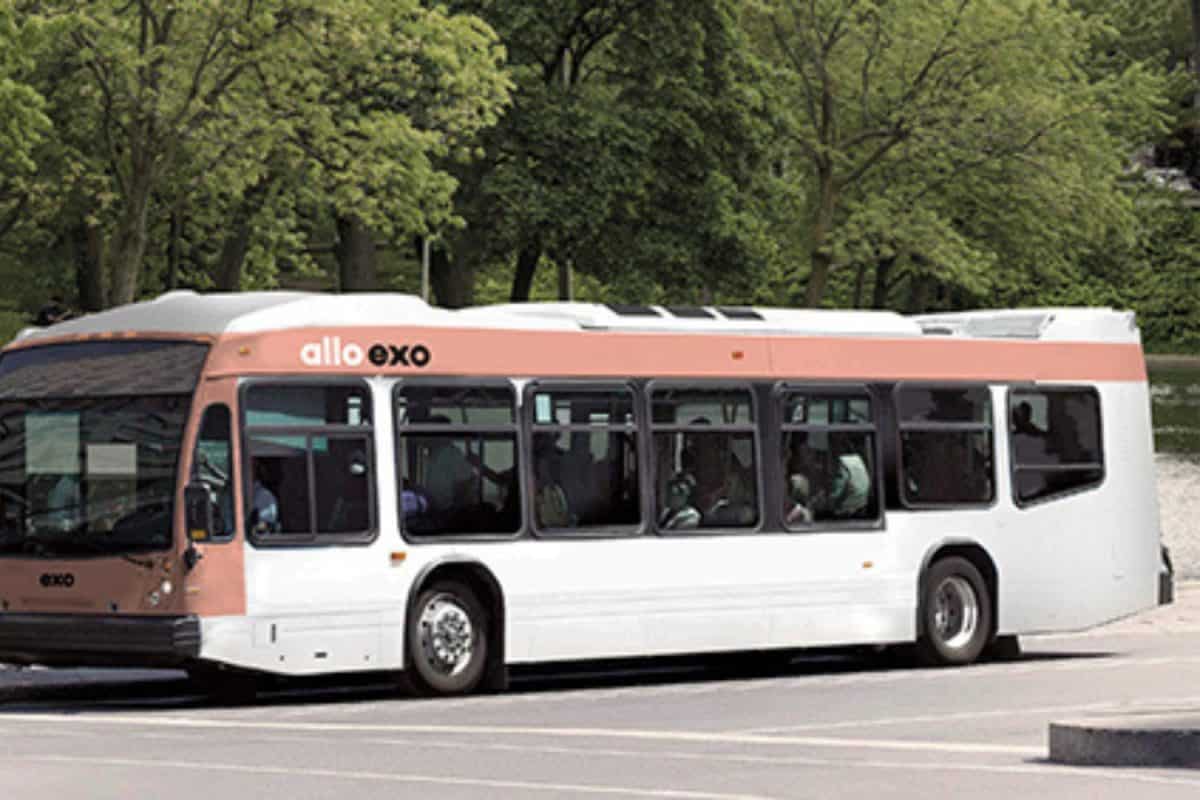 Autobus exo blanc et rose stationné sur une route bordée d’arbres verts, avec fenêtres alignées et environnement urbain calme.