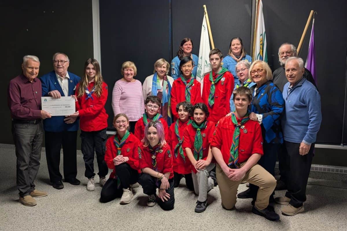 Groupe réuni dans une salle devant des drapeaux; certains tiennent un chèque, plusieurs portent des foulards et chemises rouges.