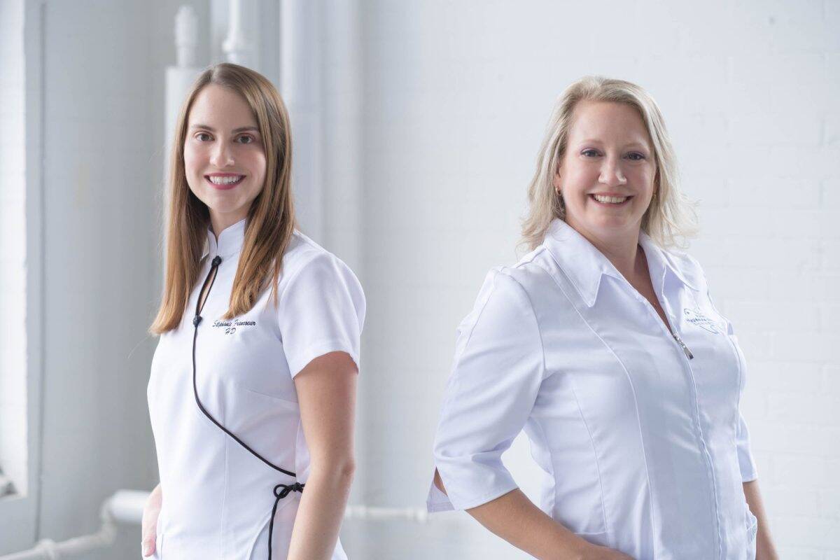 Stéphanie Francoeur et Fannie Leblanc en uniformes blancs posent dans un studio lumineux aux murs clairs, avec tuyaux apparents et éclairage doux en arrière-plan.