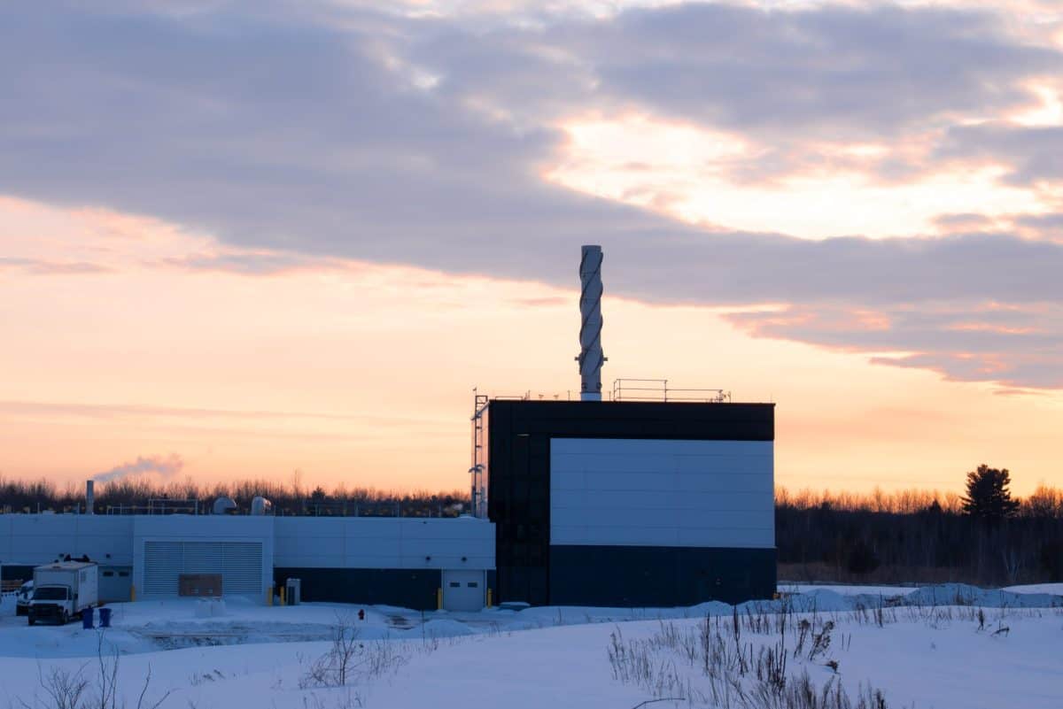 Bâtiment industriel de l’usine d’épuration de Terrebonne, entouré de neige, avec une haute cheminée sous un ciel au coucher du soleil.