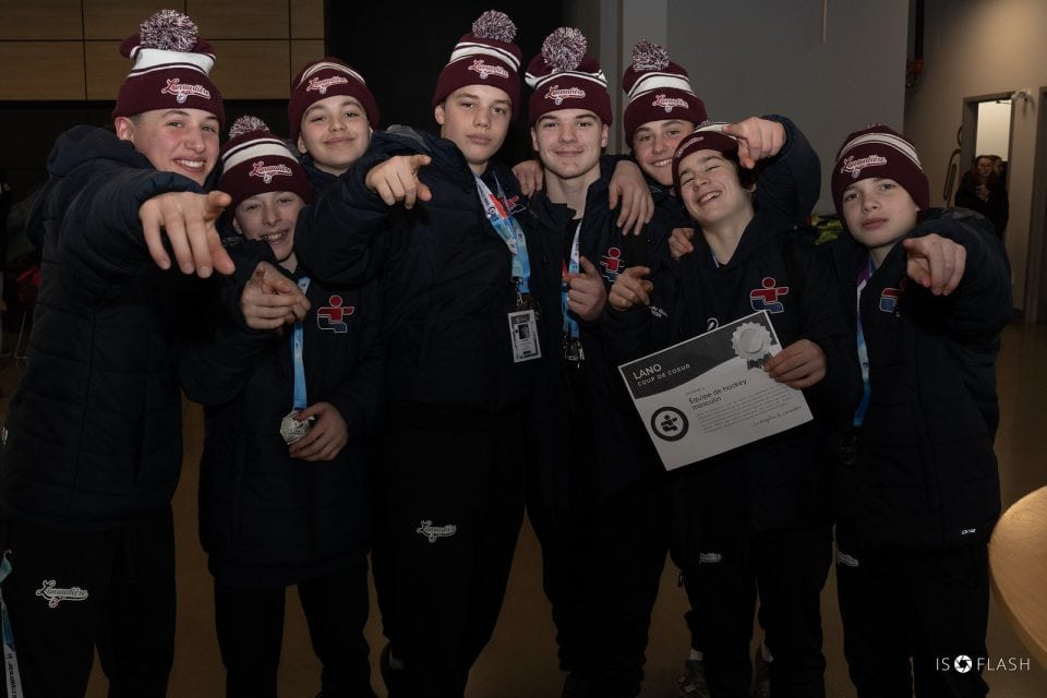 Groupe réuni à l’intérieur; médailles au cou, certificat en main, ambiance d’équipe après une compétition sportive.