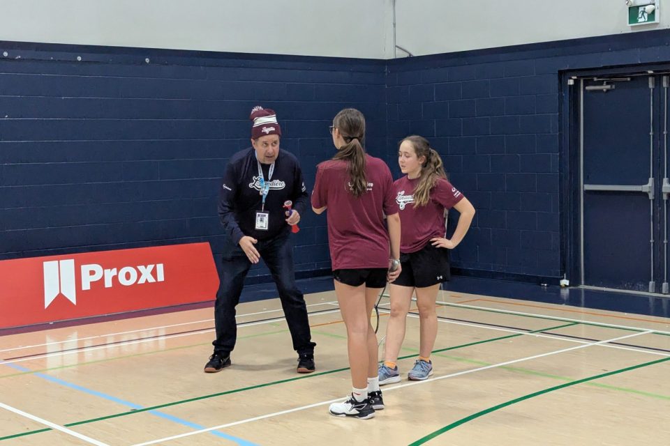 Martin Villeneuve échange avec deux joueuses sur un terrain de badminton pendant un match.