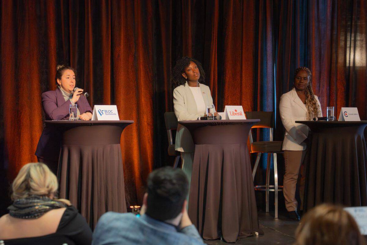 Trois femmes participent à un débat public assis derrière des tables avec des microphones et des noms