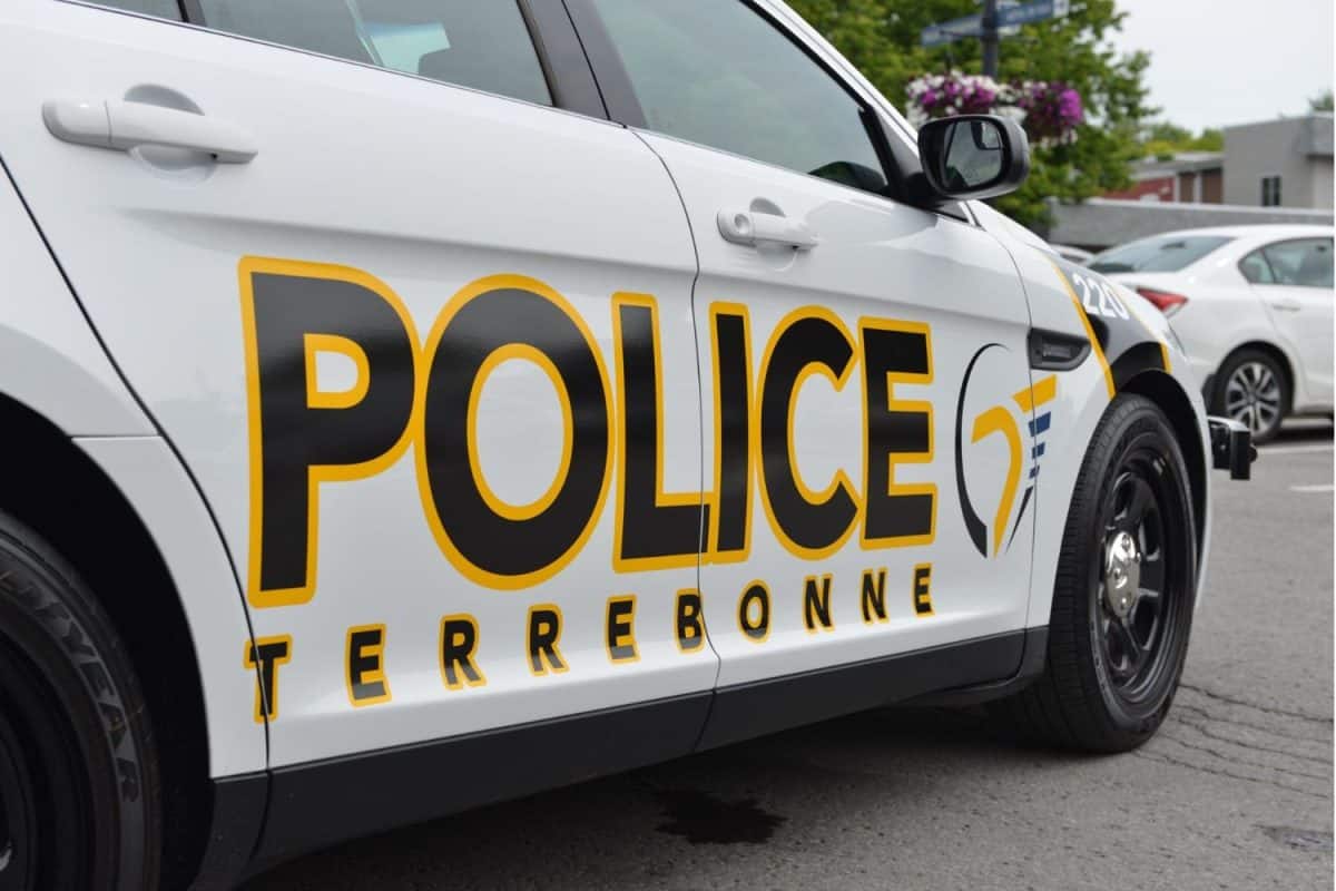 Véhicule de police blanche avec inscription jaune et noire stationnée dans un lot avec d'autres véhicules