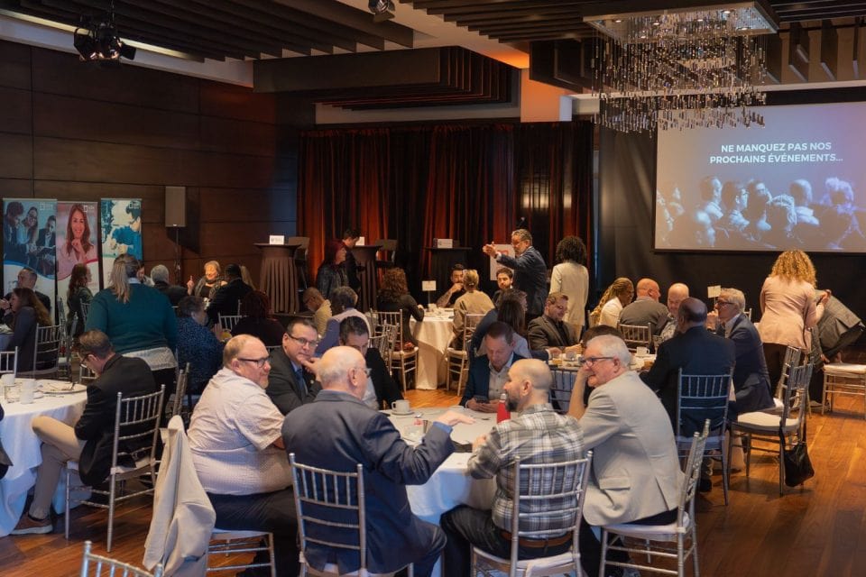 Salle d'événement avec tables de dîner, chandelier et présentation vidéo sur écran mural projetée