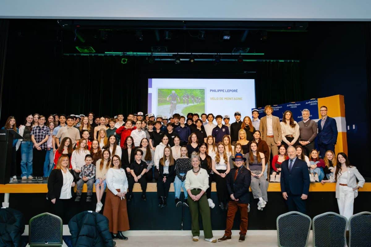 Groupe important de participants sur scène lors de présentation conférence avec écran vidéo en arrière
