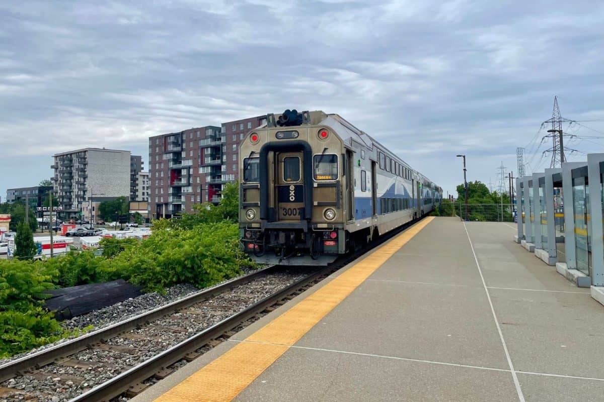 Un train bleu et beige arrive en gare dans un environnement urbain avec des immeubles résidentiels