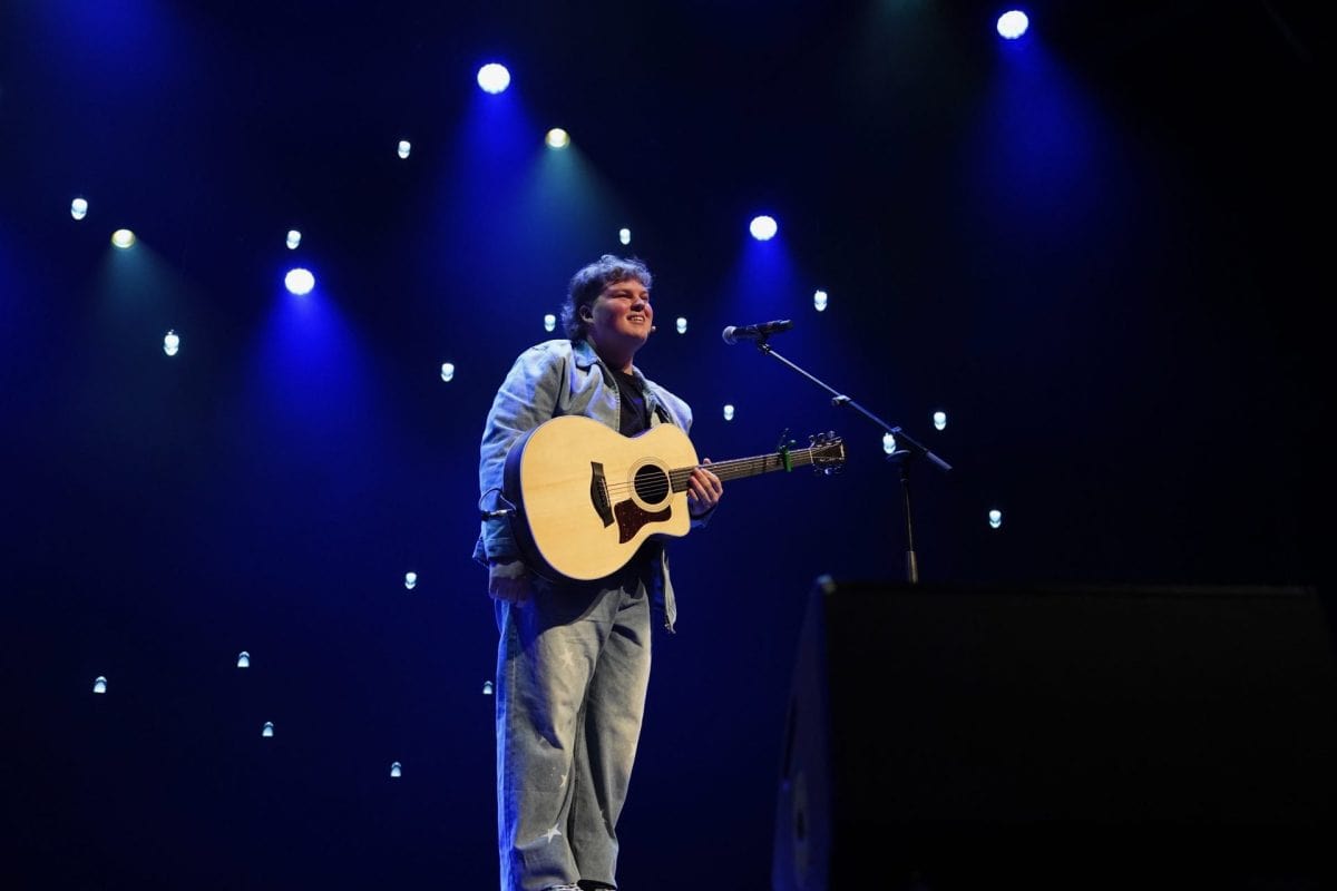 Scène de spectacle avec micro et guitare, éclairée par des lumières bleues suspendues, créant une ambiance sombre et artistique.
