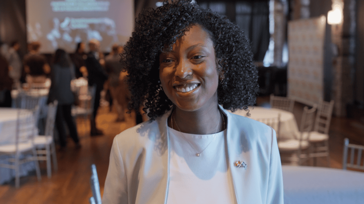 Salle intérieure avec tables rondes, chaises blanches et écran de projection en arrière-plan, dans une ambiance de réception ou événement formel.