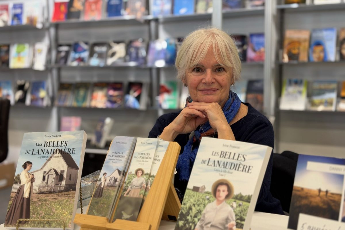 Table avec plusieurs livres exposés sur des supports, devant des étagères remplies d’ouvrages dans un espace intérieur de type librairie ou salon.