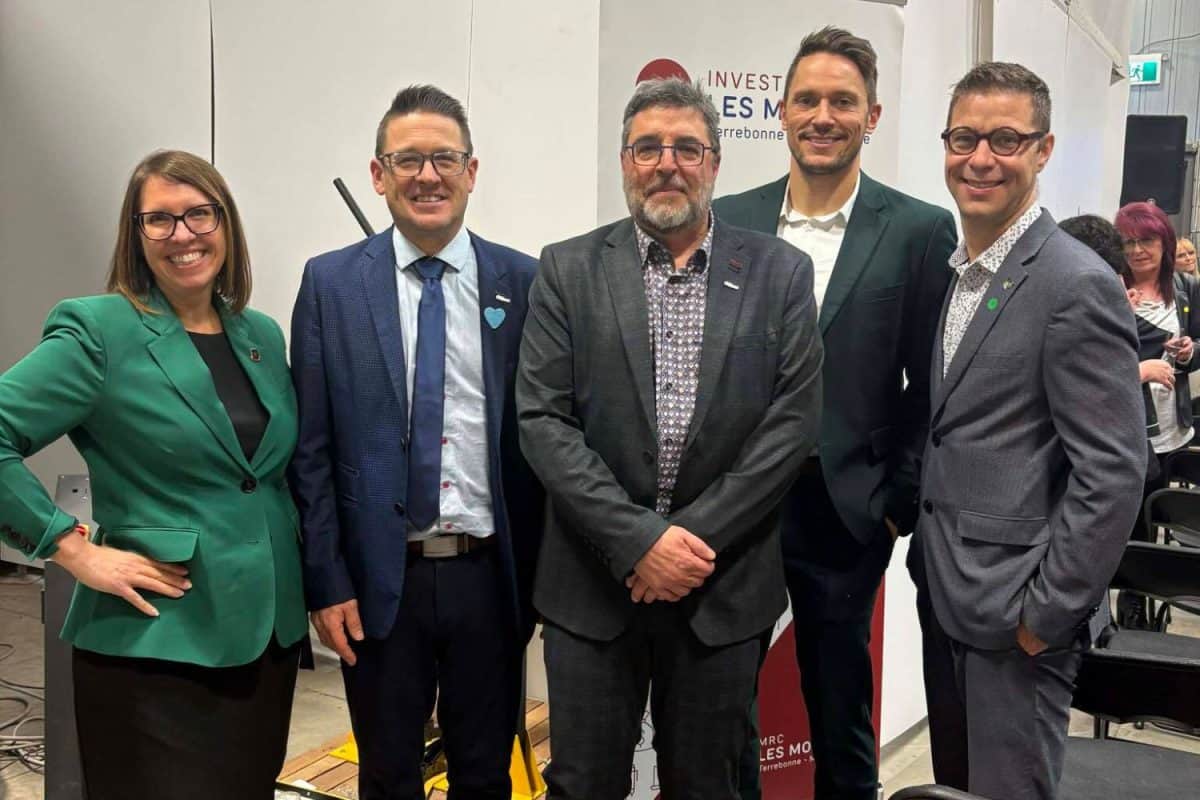 Groupe de cinq personnes posant devant une bannière d'Investir Les Moulins lors d'un événement économique régional