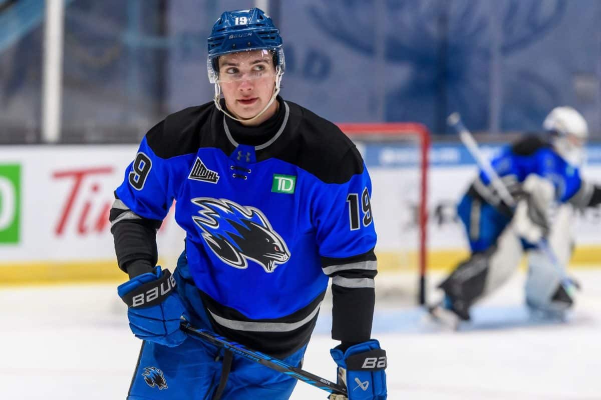 Joueur de hockey numéro 19 en position d'attaque sur la patinoire, gardien de but posté devant son filet en arrière-plan