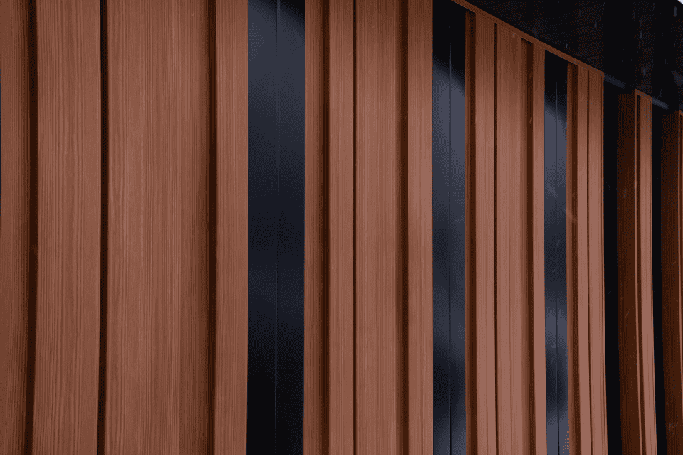 Façade moderne composée de panneaux verticaux brun texturé et bandes sombres, surface répétitive avec lignes régulières et ambiance extérieure.