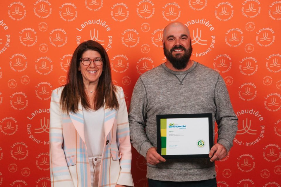 Deux personnes devant un fond orange avec logos, tenant un certificat encadré dans un contexte d’événement officiel.