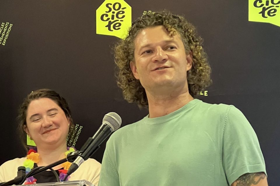 Conférencier au micro devant le fond de scène de La Nouvelle Société lors du dévoilement de la programmation estivale