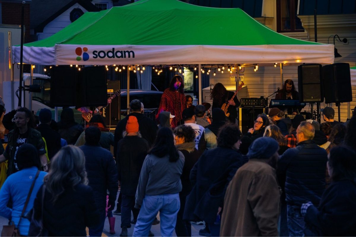 Concert de musique en soirée au Festival Grande Tribu, foule rassemblée devant une scène extérieure sous un chapiteau SODAM