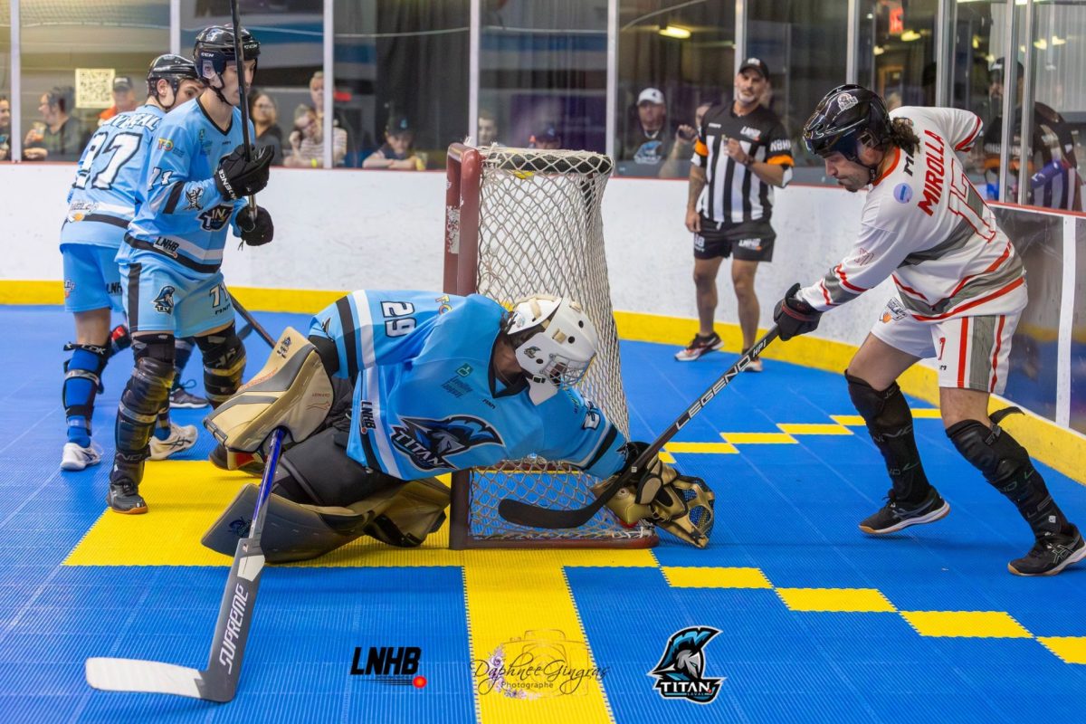 Match de hockey-balle en aréna où un gardien bloque un tir près du filet pendant une action intense devant les spectateurs.