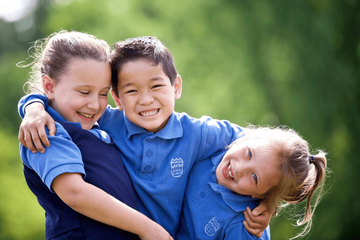 Trois enfants enlacés à l’extérieur, devant un fond de verdure flou, sous une lumière naturelle douce.
