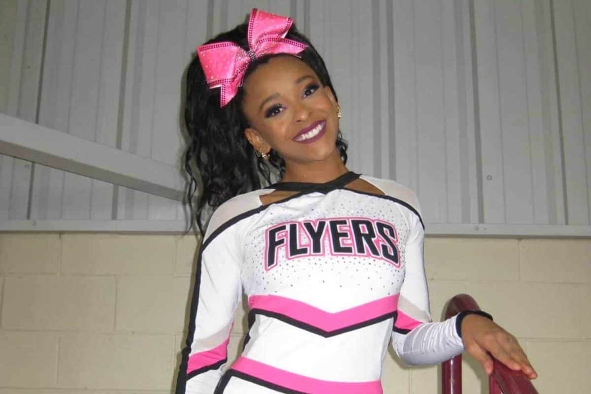 Cheerleadeuse en uniforme Flyers rose et blanc appuyée sur une rampe dans une salle sportive éclairée