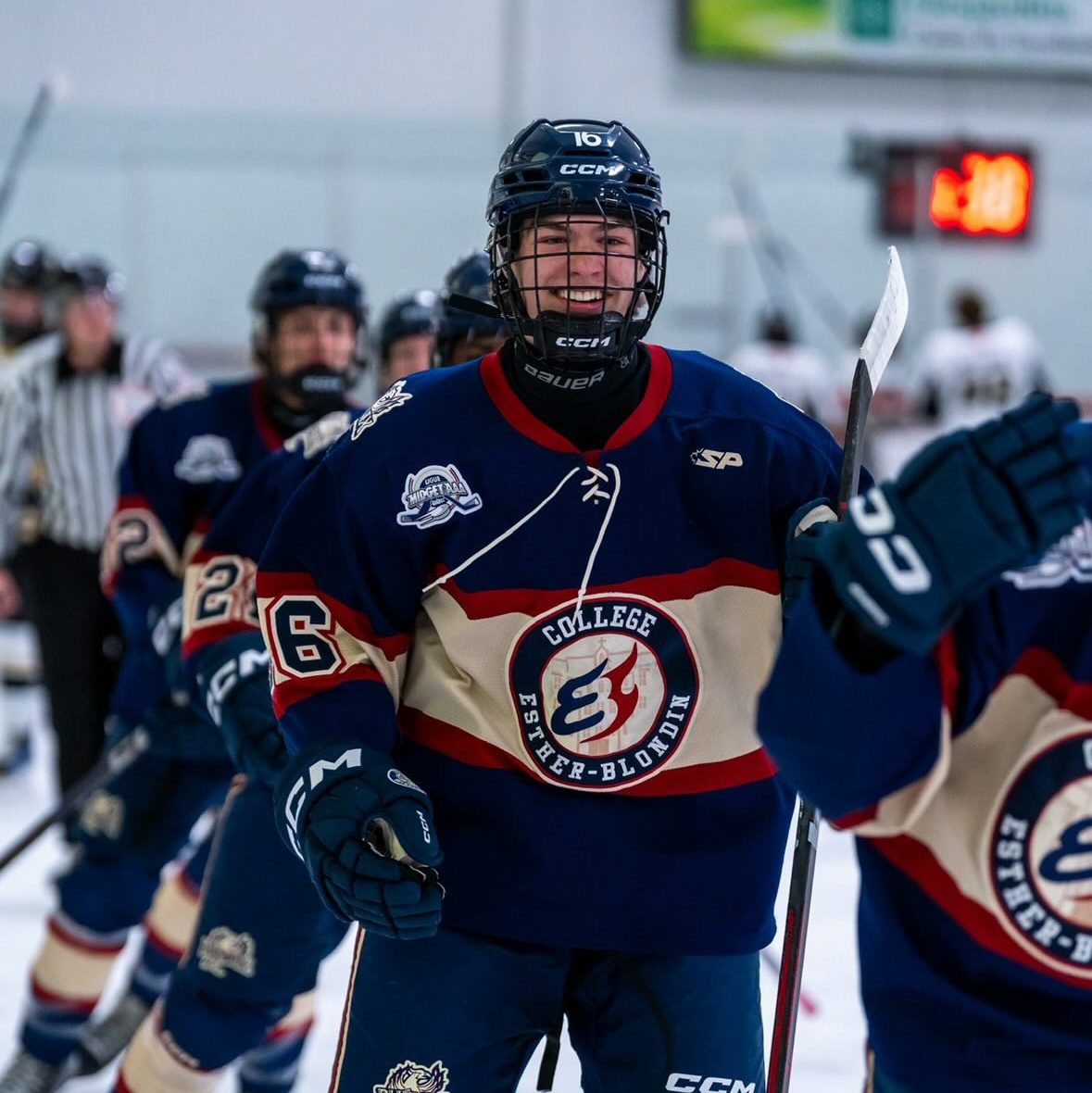 Joueur du Phénix du Collège Esther-Blondin patinant sur la glace lors d'un match de hockey, bâton levé en signe de célébration