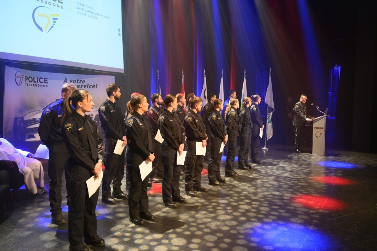 Groupe de policiers en uniforme alignés sur une scène éclairée lors d’une cérémonie officielle avec drapeaux et pupitre.