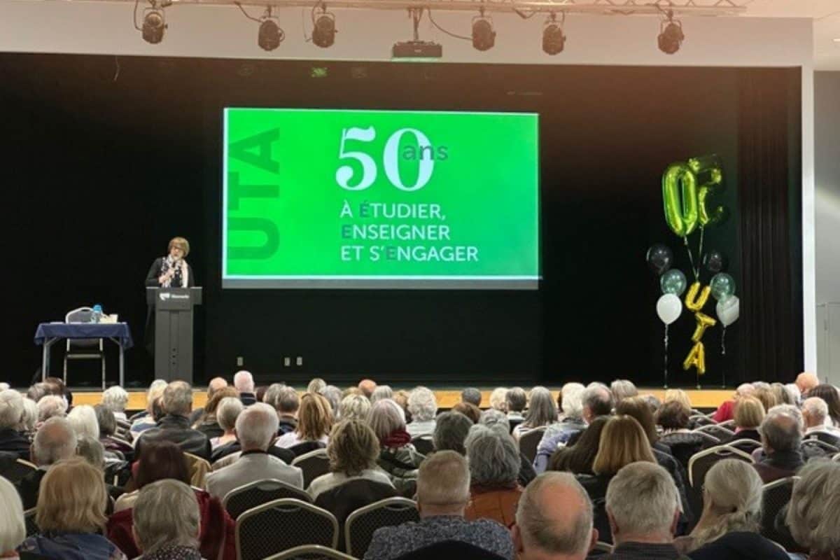 Grande salle comble pour le 50e anniversaire de l'UTA à Mascouche, projection verte avec slogan de l'événement