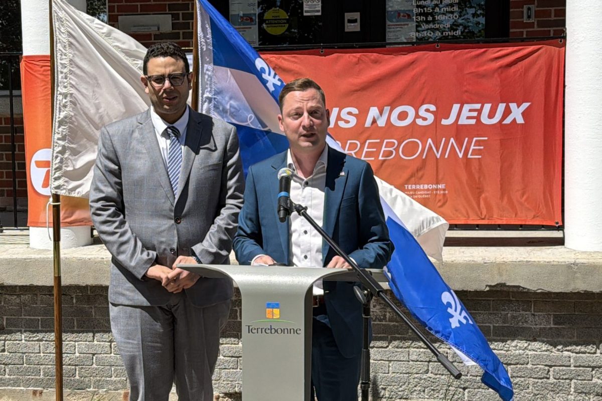 Point de presse extérieur devant l’hôtel de ville de Terrebonne, avec drapeaux du Québec et bannière promotionnelle en arrière-plan.