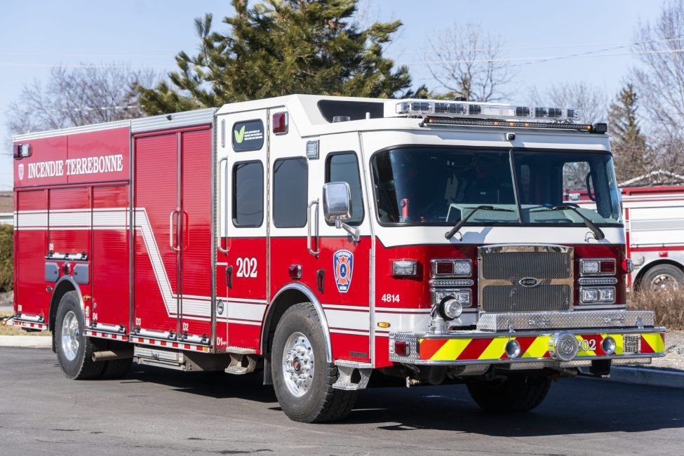 Camion d’incendie rouge stationné à l’extérieur par temps clair. Le véhicule d’intervention occupe l’avant-plan, avec des arbres et d’autres camions visibles en arrière-plan.
