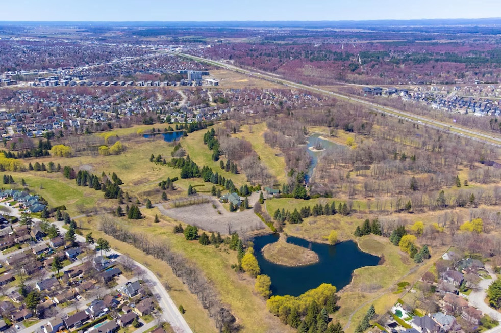 Vue aérienne d'un vaste espace vert parsemé d'étangs et de boisés en bordure d'un quartier résidentiel au printemps