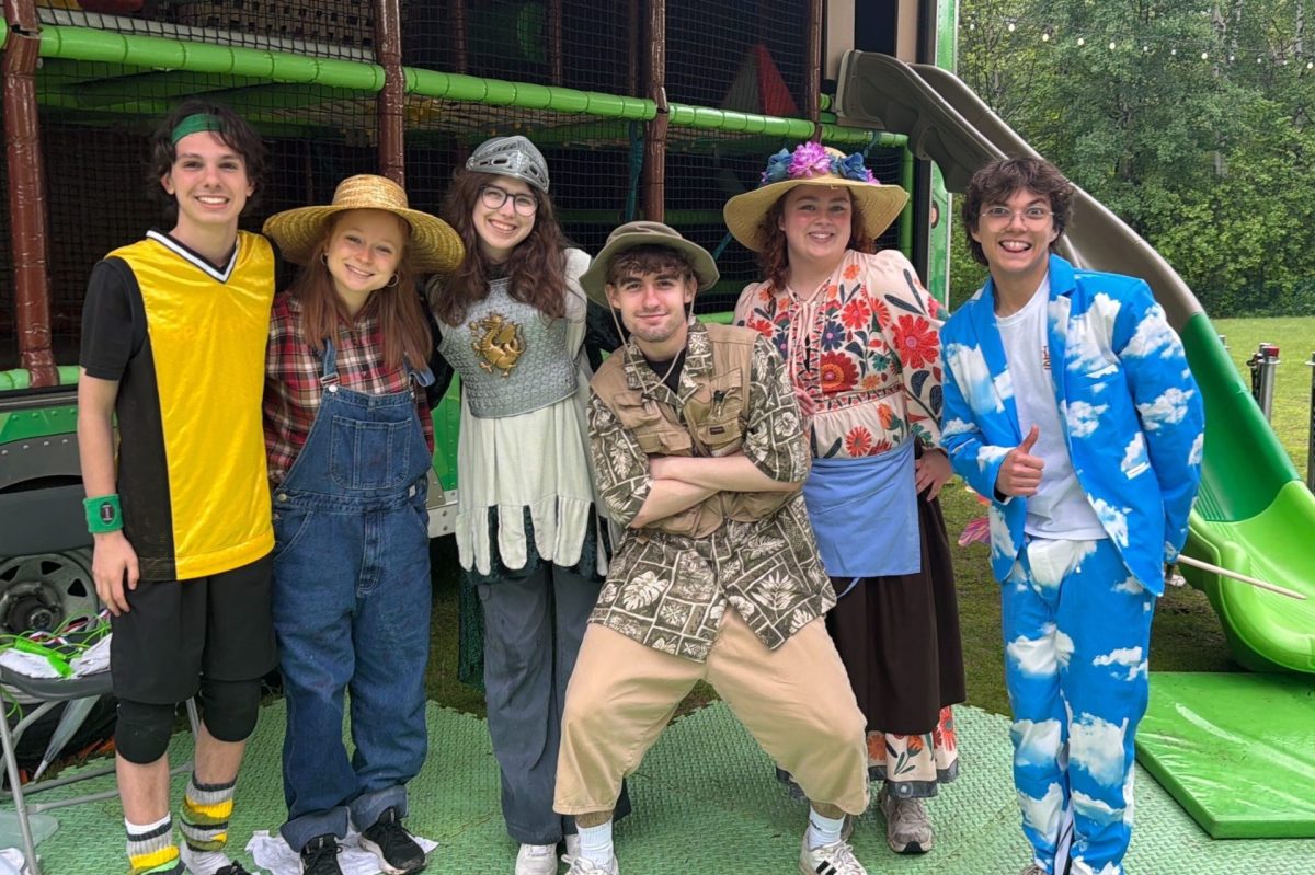 Groupe d’animateurs costumés pose devant une structure de jeux gonflable avec glissade verte dans un parc extérieur