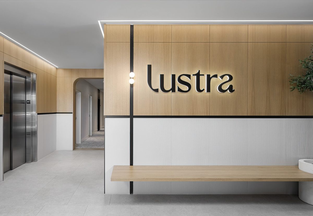 Hall d'accueil moderne, logo « Lustra » sur mur en bois clair, banc en bois et ascenseur métallique à gauche