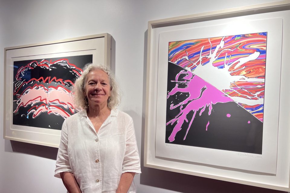 Personne posant dans une galerie d'art entre deux sérigraphies colorées encadrées aux motifs abstraits éclaboussés