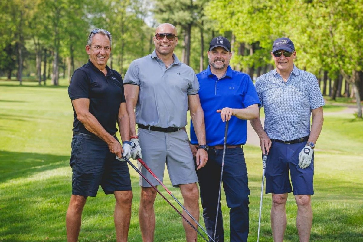 Quatre golfeurs souriants posant avec leurs bâtons sur un parcours de golf verdoyant bordé d'arbres par temps ensoleillé