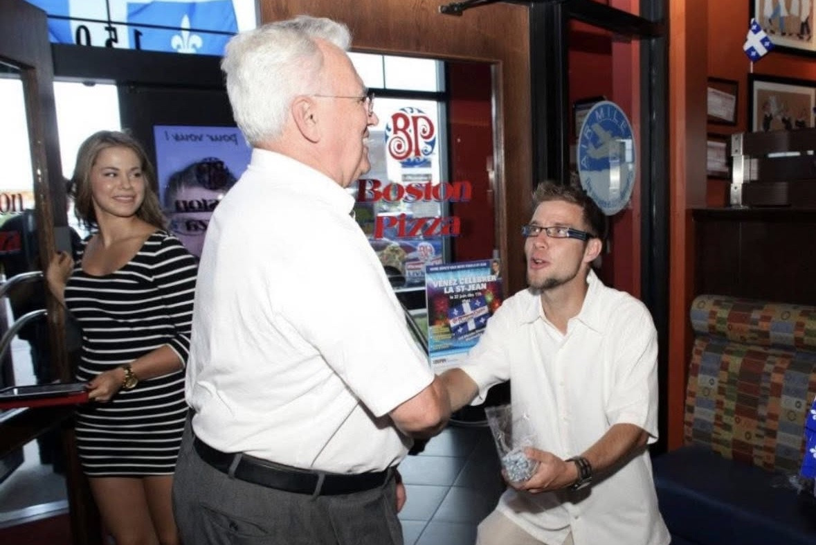 Poignée de main chaleureuse entre deux personnes à l'entrée d'un restaurant orné de drapeaux du Québec
