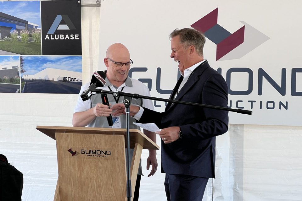 Deux intervenants au podium lors du lancement d'un chantier devant les bannières d'Alubase et de Guimond Construction
