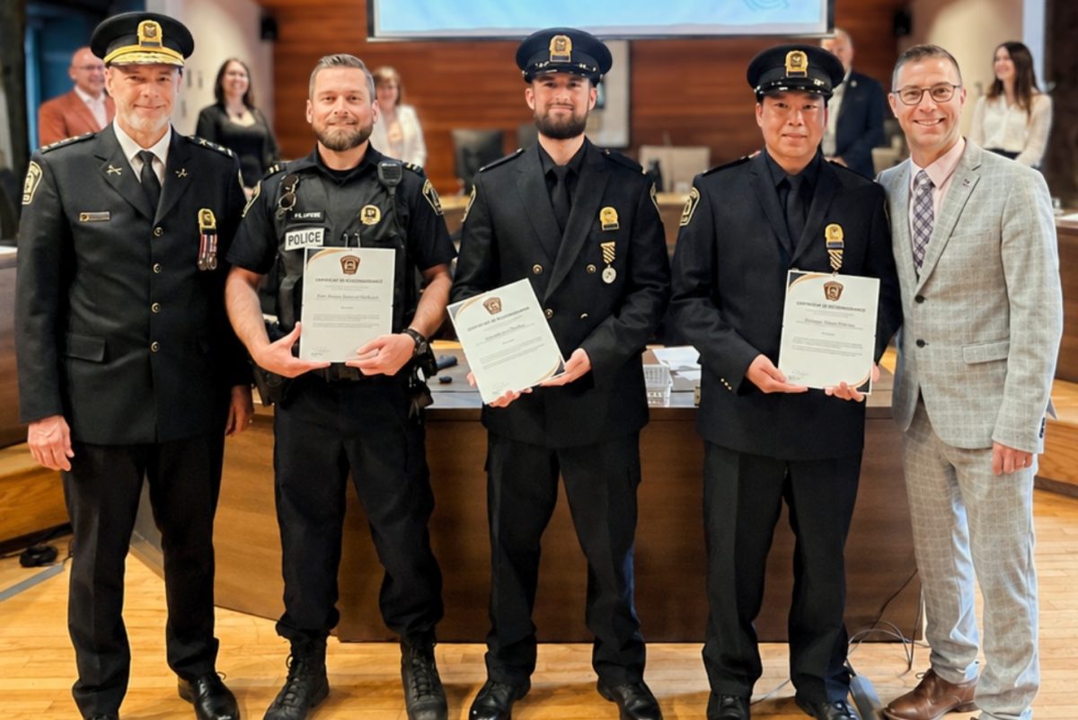 Cérémonie de remise de certificats de reconnaissance à trois agents de police posant dans une salle de conseil municipal
