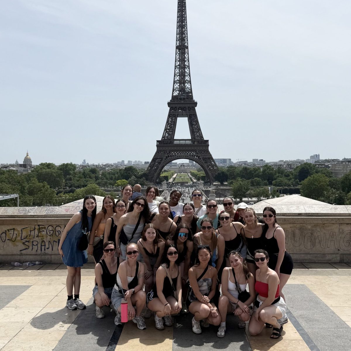 Groupe en voyage devant la tour Eiffel, réuni sur une terrasse panoramique. Le monument domine l’arrière-plan avec les jardins et la ville de Paris au loin.