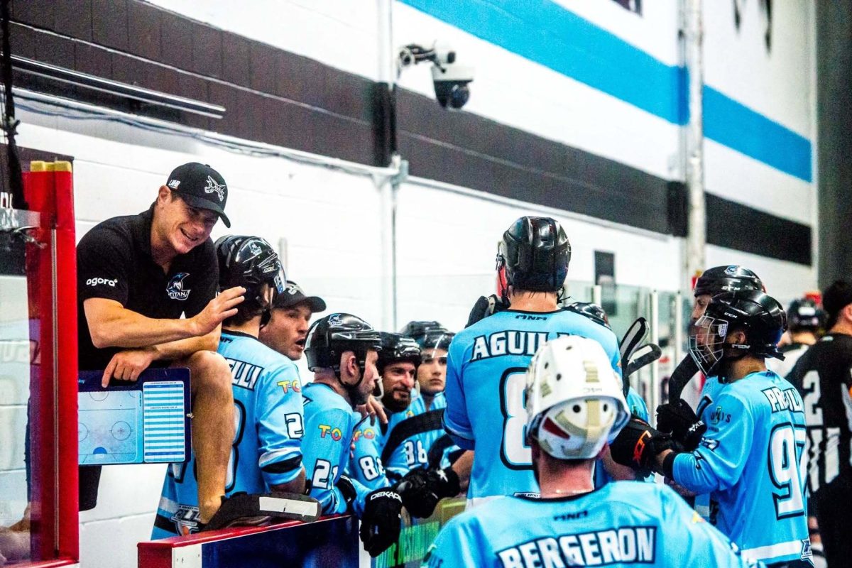 Entraîneur penché vers des joueurs casqués en patinoire, tenant un tableau tactique lors d'une pause de match