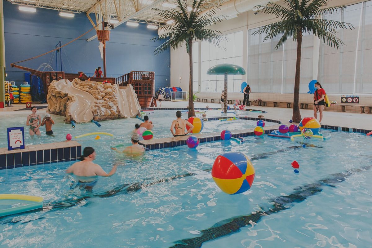 Parc aquatique intérieur avec piscine animée, balles colorées, palmiers artificiels et structure de jeu en bateau pirate