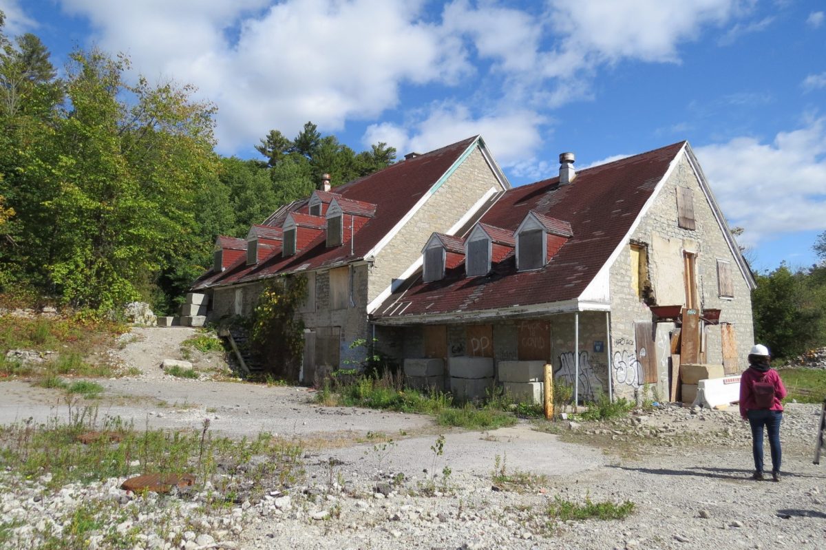 Bâtiment en pierre abandonné couvert de graffitis, fenêtres condamnées, entouré de végétation sous un ciel nuageux