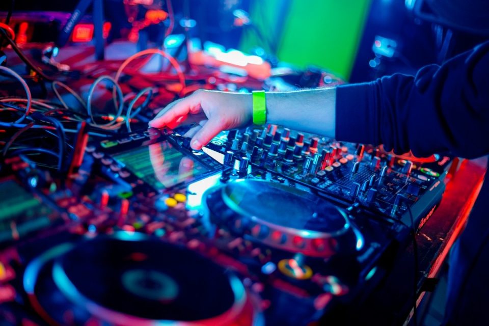 Une main manipule une table de mixage Pioneer avec platines vinyles sous des lumières colorées rouge et bleue