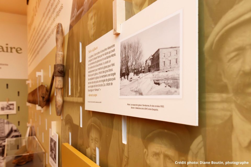 Panneau d'exposition muséale sur la coupe de glace à Terrebonne, avec photo ancienne et outils en bois accrochés au mur