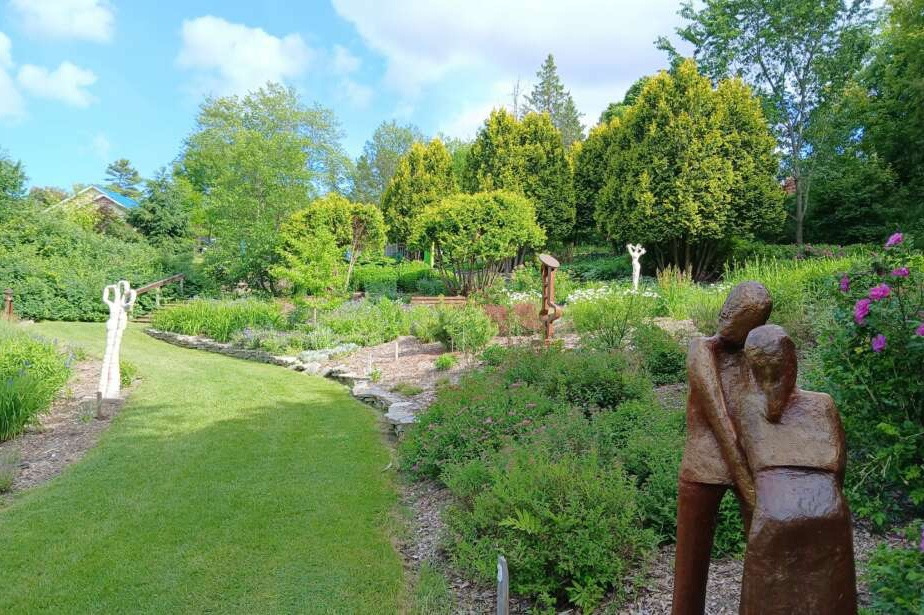 Jardin de sculptures en plein air, œuvres en métal rouillé et bois parmi des massifs fleuris et arbres verdoyants