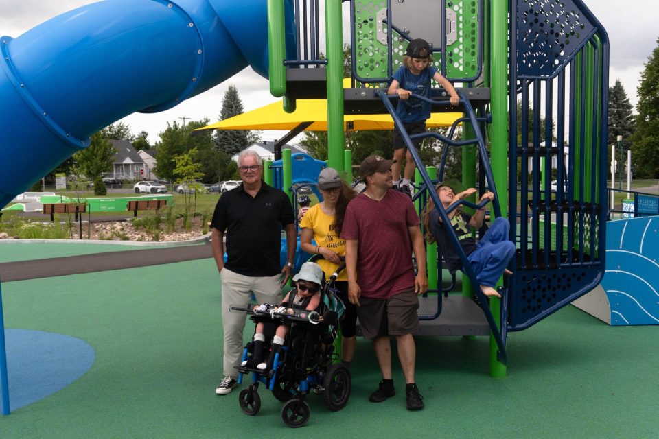 Aire de jeux inclusive colorée où des enfants grimpent, un fauteuil roulant visible, sous un ciel nuageux