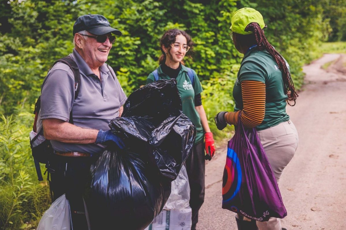 Bénévoles ramassant des déchets sur un sentier verdoyant, munis de sacs noirs et de gants, par une journée ensoleillée