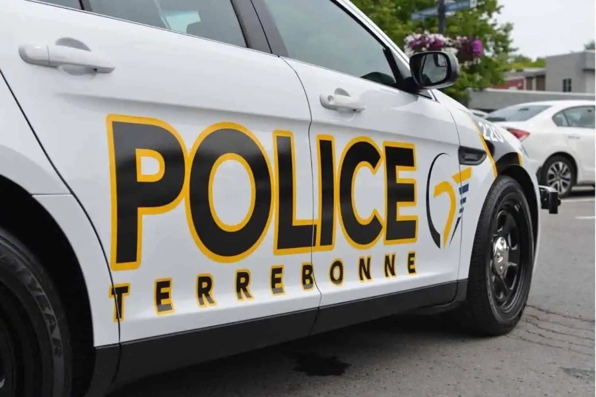 Véhicule de patrouille blanc de la Police de Terrebonne stationné dans un stationnement, avec arbres et fleurs en arrière-plan