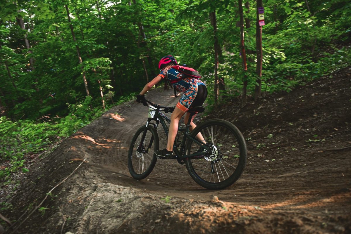 Un cycliste négocie un virage serré sur un sentier de VTT en terre, entouré d'une dense forêt verdoyante en été