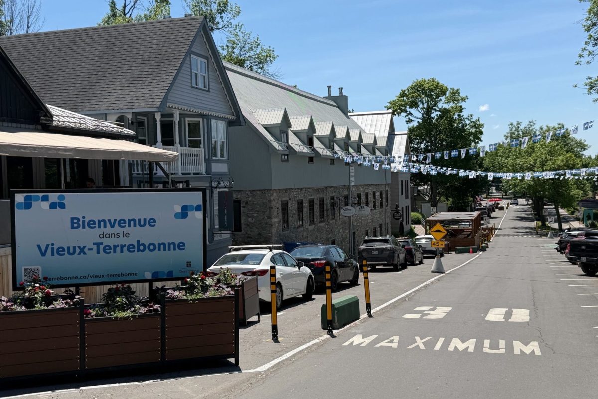 Rue du Vieux-Terrebonne ensoleillée, bâtiments historiques en pierre et drapeaux du Québec en guirlande